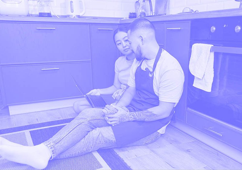a man and woman sitting on the floor in a kitchen