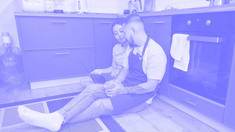 a man and woman sitting on the floor in a kitchen